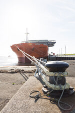 Ein rotes Frachtschiff ist mit einem Seil an einem Schiffspoller an Land befestigt.
