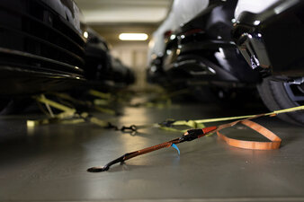 Mehrere schwarze Autos stehen nebeneinander und sind mit Zurrgurten am Boden eines Car Carriers befestigt.