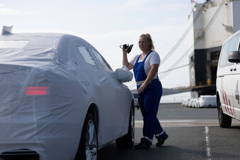 Eine Mitarbeiterin steht vor einem in Schutzfolie umhülltes Auto, das vor dem Car Carrier steht.