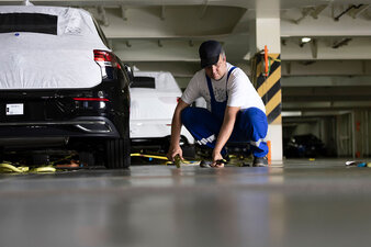Ein Mitarbeiter kniet neben einem Auto und befestigt dieses mit Karabinern zum sicheren Weitertransport auf einem Car Carrier.