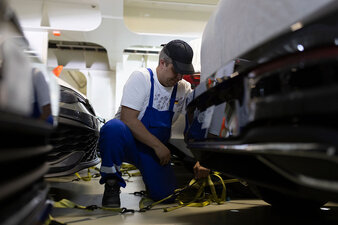 Ein Mitarbeiter kniet neben zwei Autos und befestigt diese mit Karabinern zum sicheren Weitertransport auf einem Car Carrier.