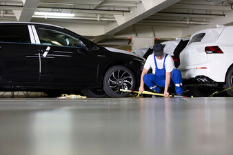 Ein Mitarbeiter kniet neben einem Auto und befestigt dieses mit Karabinern zum sicheren Weitertransport auf einem Car Carrier.