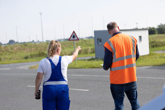 Zwei Mitarbeiter in Arbeitskleidung stehen vor einer grünen Wiese und schauen in die Ferne.