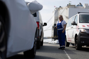 Eine Mitarbeiterin die zwischen zwei Transportern steht. Im Hintergrund sieht man den Car Carrier.