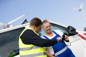 Zwei Personen stehen vor einem Transporter und schauen auf ein Scangerät. 